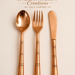 May include: A set of polished copper cutlery consisting of a spoon, a fork, and a knife with banded handles. The text INDIANHERIT Creations FULL COPPER is displayed above the utensils, which feature a metallic finish and a smooth, reflective surface.
