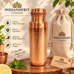 May include: A hammered copper water bottle with a matching screw-top lid, accompanied by a beige drawstring fabric pouch featuring the Indianherit Creations logo and a matching brown paper tag with the same brand name and lotus flower icon.