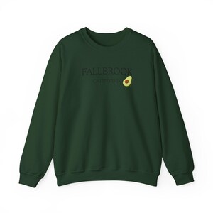 May include: A dark green sweatshirt with the text "FALLBROOK CALIFORNIA" in a simple font. A small avocado graphic is to the right of the text. The sweatshirt has long sleeves and a crew neck.