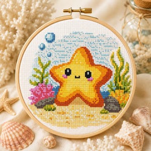 Pode incluir: Um bastidor de bordado circular de madeira contendo um padrão de ponto cruz de uma estrela-do-mar amarela sorridente. O design apresenta coral rosa, algas verdes, bolhas azuis e um fundo arenoso em tecido branco com parafuso de metal.