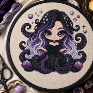 Pode incluir: Um bordado em ponto cruz num bastidor circular preto apresentando uma personagem estilo chibi com cabelo comprido roxo e preto, olhos grandes e vestido preto, rodeada por tentáculos escuros, conchas roxas e pequenas bolhas em tecido bege.