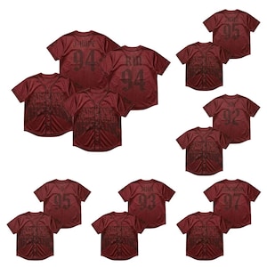 May include: A collection of maroon button-down baseball jerseys featuring short sleeves and a dark graphic print on the front. Each jersey displays a unique name and number on the back, including J-Hope 94, RM 94, Jimin 95, Jin 92, V 95, Suga 93, and Jungkook 97.