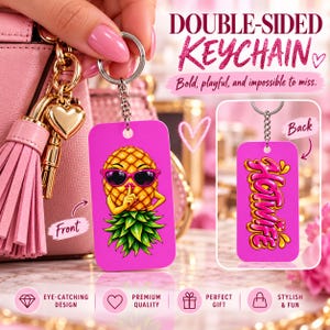 May include: A double-sided rectangular keyring with a bright pink background. The front features a cartoon pineapple wearing pink sunglasses and making a shushing gesture. The back displays the text Hotwife in stylised pink and yellow lettering.