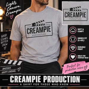 May include: A heather gray short-sleeve t-shirt featuring a black graphic of a film clapperboard and the text "CREAMPIE PRODUCTION" in a rectangular frame. The shirt has a crew neckline and a standard fit, displaying the logo clearly on the chest.
