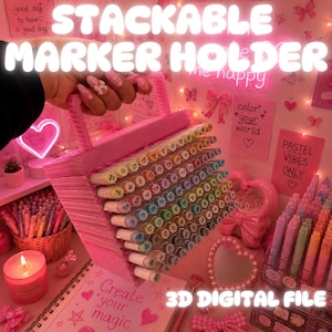 Puede incluir: Un soporte para marcadores apilable impreso en 3D de color rosa con asa, diseñado para almacenar numerosos marcadores en un patrón de cuadrícula. El soporte está lleno de marcadores de varios colores, mostrando cada tapa y etiqueta.