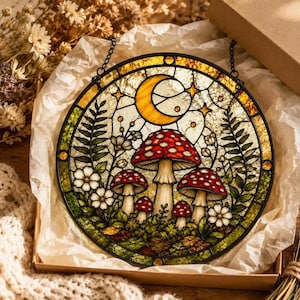 Op de afbeelding: Een ronde glas-in-lood zonnevanger met een bossc&egrave;ne van rood-witte paddenstoelen, groene varens en kleine witte bloemen. In het bovenste gedeelte zijn een gele halve maan en sterren afgebeeld. Het object heeft een zwart metalen frame.