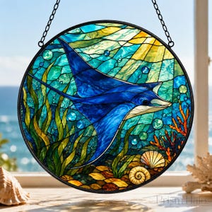 May include: A circular stained glass suncatcher featuring a deep blue manta ray swimming through an underwater scene with green seaweed, orange coral, and seashells. The background includes blue water textures and yellow sunlight rays.