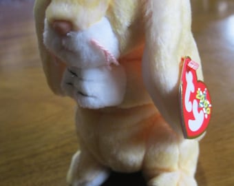 May include: A plush toy rabbit with soft, pale yellow fur and white accents on the face and paws. The rabbit has long, floppy ears and a small pink nose. A red heart-shaped tag with the white letters TY and the year 2009 is attached to the ear.