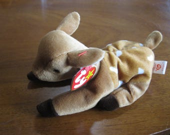 Peut inclure: Une peluche en forme de faon avec une fourrure beige, des taches blanches sur le dos et des sabots marron foncé. Le jouet porte une étiquette rouge en forme de cœur Ty sur l'oreille et une étiquette blanche avec l'inscription Whisper.