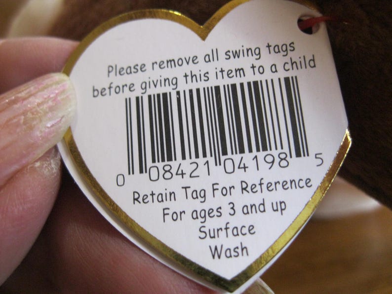 May include: A heart-shaped white swing tag with a gold border featuring a barcode and the text: Please remove all swing tags before giving this item to a child. Retain Tag For Reference. For ages 3 and up. Surface Wash. The tag has a small hole.