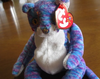 Peut inclure: Une peluche en forme de chat avec un motif tie-dye multicolore composé de fourrure bleue, violette et rose. Le chat possède un poitrail blanc uni, des pattes blanches et une étiquette rouge en forme de cœur Ty Beanie Baby à l'oreille gauche.