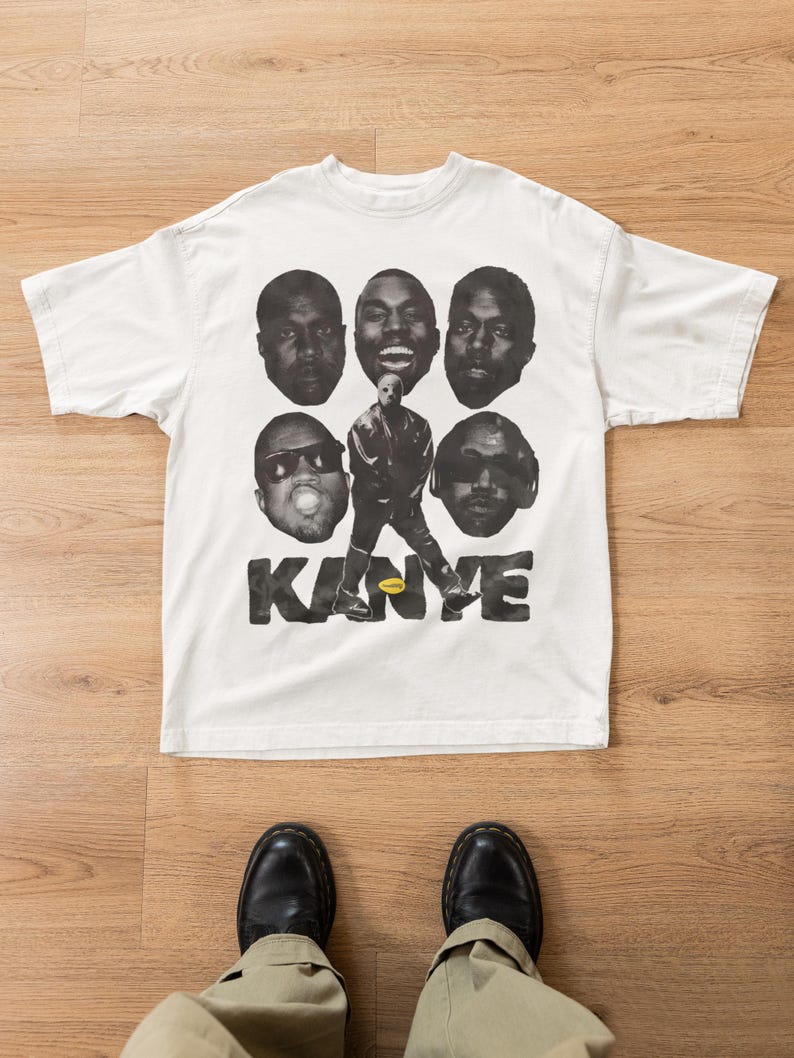 Pode incluir: Uma t-shirt branca de manga curta com uma impress&atilde;o gr&aacute;fica a preto e branco de cinco retratos de Kanye West rodeando uma figura central com uma m&aacute;scara. O nome KANYE est&aacute; impresso em letras pretas grandes com um pequeno oval amarelo.