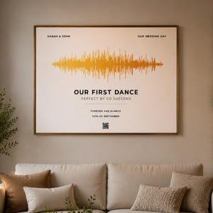 May include: A rectangular wall art print in a thin gold frame featuring a horizontal gold sound wave graphic on a white background. Text includes SARAH & JOHN, OUR WEDDING DAY, OUR FIRST DANCE, PERFECT BY ED SHEERAN, FOREVER AND ALWAYS, 15TH OF SEPTEMBER, and a QR code.
