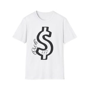 Puede incluir: Camiseta blanca con un gran símbolo de dólar negro. La palabra "Rich" está escrita en cursiva encima del símbolo del dólar, con "777" debajo. Una camiseta informal.
