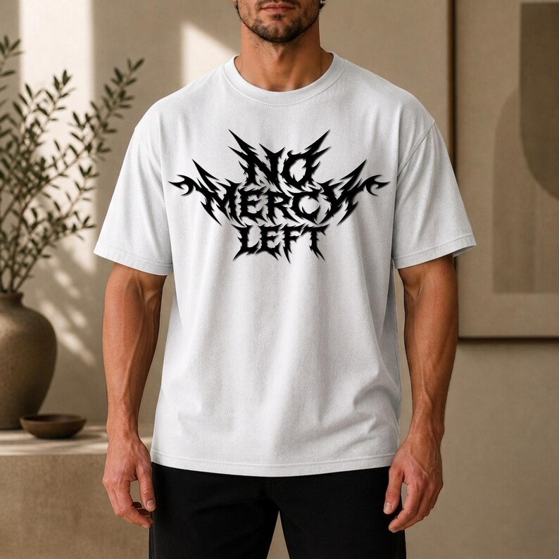 May include: A white short-sleeved t-shirt featuring a black graphic print on the chest. The design consists of the text "NO MERCY LEFT" written in a sharp, jagged, metal-inspired font with decorative spikes extending from the lettering.