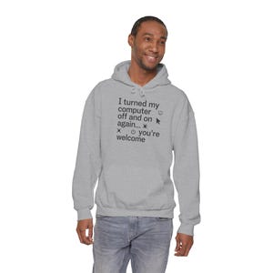 May include: A light gray hooded sweatshirt featuring dark gray text that reads: I turned my computer off and on again... you're welcome. The design includes a small computer mouse cursor icon, a power button symbol, and decorative pixelated shapes.