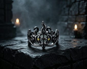 Op de afbeelding: Een donkere metalen ring met een ingewikkeld opengewerkt ontwerp met vlamachtige motieven en een centraal verticaal element. Twee kleine, ronde, gele edelstenen zijn symmetrisch aan weerszijden van het midden geplaatst voor een kleuraccent.
