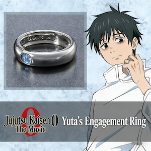 May include: A silver-toned metal ring featuring a small, round, light blue stone set into the band. The interior of the band is engraved with the text "©KP ©GA/S B.". The ring is displayed alongside an illustration of an anime character.
