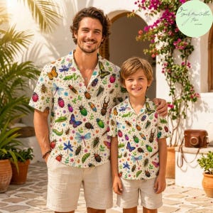 May include: A short-sleeved button-down shirt featuring a colorful insect and butterfly pattern on a cream background. The shirt has a classic collar and a straight hem, showcasing various beetles, dragonflies, and moths in vibrant colors.