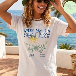 Peut inclure: Un t-shirt blanc &agrave; manches courtes avec le texte bleu "EVERY DAY IS A SUN DAY" au-dessus d'un soleil jaune et d'une illustration de corde &agrave; linge verte avec des maillots de bain et des lunettes. Le texte "WITH A CHANCE OF SUN" et "MOSTLY SUNNY" est inscrit en dessous.