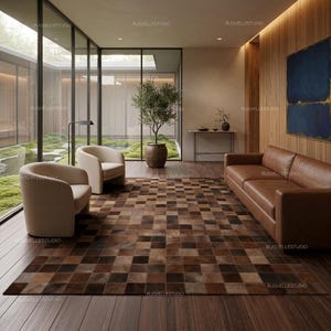 Puede incluir: Una alfombra rectangular grande con un diseño de mosaico de cuadrados en varios tonos de marrón, beige y chocolate. La alfombra está colocada sobre un suelo de madera oscura en una habitación con dos sillones beige y un sofá de cuero marrón.