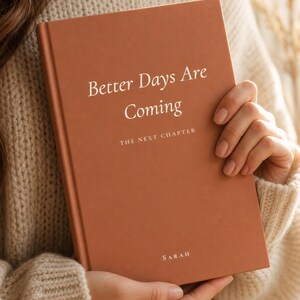 Peut inclure: Un journal à couverture rigide de couleur terre cuite avec le texte imprimé en blanc Better Days Are Coming, THE NEXT CHAPTER, et le nom SARAH en bas. Le livre présente une finition mate lisse et est tenu verticalement.