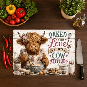 Peut inclure: Une planche à découper rectangulaire illustrée d'une vache Highland poilue portant un tablier à fleurs et mélangeant de la pâte dans un bol. Le texte indique BAKED WITH LOVE & A LITTLE COW ATTITUDE, avec un fouet, un pot de farine et des biscuits.