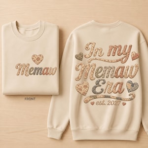 May include: A beige crewneck sweatshirt featuring a front design with the word Memaw and a heart, and a back design with the text In my Memaw Era est. 2027 surrounded by various patterned hearts. The lettering and hearts have a brown patchwork print.