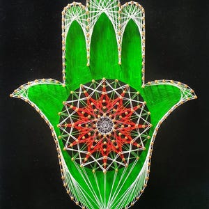Könnte beinhalten: Handgefertigtes Hamsa-Hand-String-Art-Stück. Die Handfläche ist grün, mit einem zentralen roten und weißen Sternmuster. Weißer Faden umreißt die Hand und den Stern, mit kleinen goldfarbenen Perlen an den Kreuzungen. Der Hintergrund ist schwarz.
