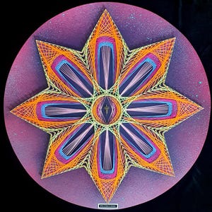 Puede incluir: Una vibrante pieza de arte de hilo que presenta un diseño de estrella. La obra de arte utiliza hilos naranjas, rosas, azules y amarillos sobre un fondo circular púrpura. La estrella tiene ocho puntas, con un diseño central.