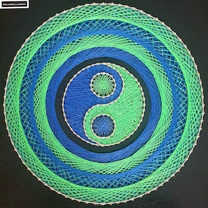 Puede incluir: Una pieza circular de arte con hilo que presenta un símbolo del Yin y Yang en tonos azules y verdes. El diseño está compuesto por círculos concéntricos y las dos mitades del símbolo son de colores distintos. El fondo es negro.