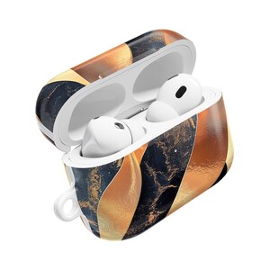 May include: A white wireless earbud charging case with an open lid, featuring a decorative pattern of dark navy blue marble textures and metallic gold curved stripes. Two white wireless earbuds are seated inside the charging case.