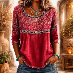May include: A long-sleeved red top featuring a scoop neckline with a white geometric pattern across the chest and shoulders. The garment is paired with blue denim jeans and accessorized with a layered turquoise stone necklace and bracelets.