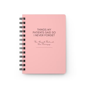 May include: A light pink spiral-bound notebook featuring the black printed text "THINGS MY PATIENTS SAID SO I NEVER FORGET" followed by the script text "The Heart Behind the Therapy" and a horizontal line centered on the front cover.