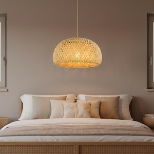 Peut inclure: Une suspension en forme de dôme dotée d'un abat-jour en bambou tressé avec un motif en losanges. La lampe diffuse une lueur chaude et douce à travers le matériau de couleur beige naturel, suspendue par un seul cordon fin depuis le plafond.