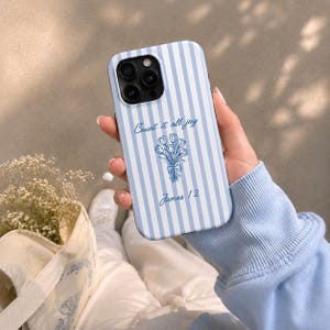 May include: A light blue and white striped phone case featuring a blue line art illustration of a tulip bouquet. The text "Count it all joy" is printed above the flowers, and "James 1:2" is printed below the bouquet in a blue script font.