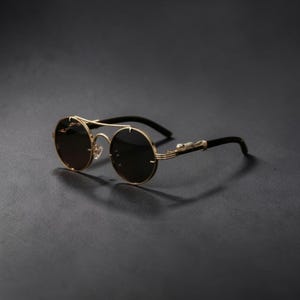 May include: Round sunglasses featuring dark lenses and a gold-tone metal frame. The bridge and temples are accented with a gold-coloured panther figure. The temple tips are black, and the frame includes a double bridge design above the lenses.