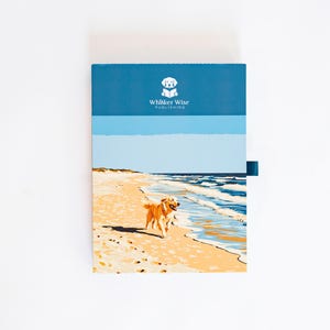 K&ouml;nnte beinhalten: Eine rechteckige Schachtel mit einem blauen oberen Bereich, der das wei&szlig;e Logo und den Text Whisker Wise Publishing zeigt. Der untere Teil zeigt eine grafische Illustration eines goldenen Hundes, der an einem Sandstrand neben blauen Wellen l&auml;uft.