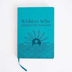 K&ouml;nnte beinhalten: Ein hellt&uuml;rkisfarbener Hardcover-Planer mit einem Lesezeichenband. Der Einband zeigt den Text "Whisker Wise LIFESPAN PET PLANNER" in Dunkelblau &uuml;ber einer Grafik einer aufgehenden Sonne &uuml;ber stilisierten Wellen mit einem Pfotenabdruck.