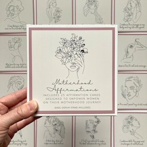 May include: A set of 25 affirmation cards with a pink background and a black and white line drawing of a woman with flowers covering her face. The text on the front of the box reads "Motherhood Affirmations" and includes the text "Includes 25 affirmation cards designed to empower women on their motherhood journey. (Easel display stand included)"