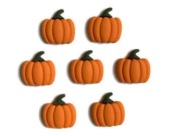 Puede incluir: Siete botones pequeños con forma de calabaza naranja dispuestos en un grupo. Cada botón presenta un cuerpo liso y redondeado con crestas verticales y un tallo verde oscuro en la parte superior. Los botones son uniformes en tamaño y color.