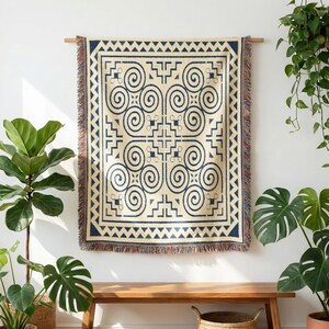 May include: A rectangular woven throw blanket featuring a cream-colored base with a dark blue geometric pattern. The design includes four large central spirals, intricate angular lines, and a triangular border. The edges have a fringed finish.