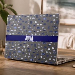 Könnte beinhalten: Eine graue Laptop-Hartschalenhülle mit einem sich wiederholenden Muster aus blauen und weißen Surfbrettern, Palmen, Meeresschildkröten und Strandsonnenschirmen. Ein dunkelblauer horizontaler Streifen in der Mitte zeigt den weißen Text JULIA.