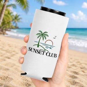 May include: White can cooler with a black top, featuring a green palm tree, a red sun, and the text "SUNSET CLUB" in black. The design is set against a beach scene with a blue ocean and sky.