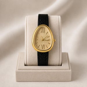May include: A wristwatch with a teardrop-shaped gold case and a textured gold dial featuring Roman numerals at the twelve and six o'clock positions. The watch has a black leather strap with a pebbled grain texture and a small gold crown on the side.