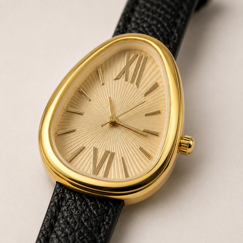 May include: A wristwatch with a gold-toned, teardrop-shaped case and a textured gold sunburst dial. The dial features Roman numerals at the twelve and six o'clock positions, simple gold indices for other hours, and a black textured leather strap.