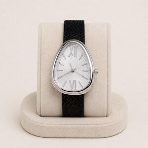 May include: A wristwatch with a teardrop-shaped silver case and a white dial featuring a sunburst pattern. The dial displays silver Roman numerals at the twelve and six o'clock positions, with simple silver hour markers. It has a black textured leather strap.