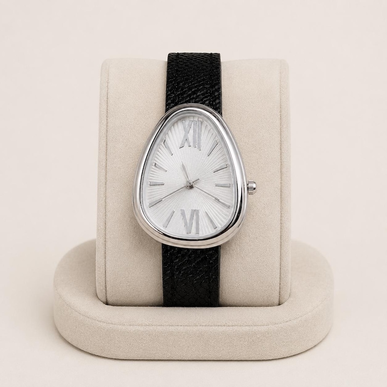 May include: A wristwatch with a teardrop-shaped silver case and a white dial featuring a sunburst pattern. The dial displays silver Roman numerals at the twelve and six o'clock positions, with simple silver hour markers. It has a black textured leather strap.