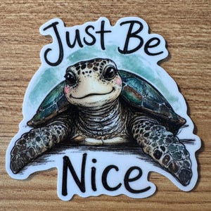 May include: A die-cut sticker featuring a detailed illustration of a smiling sea turtle with pink cheeks. The turtle has a green and brown shell and textured skin. The text "Just Be Nice" is printed in black script above and below the turtle.