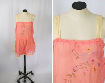 May include: A peach-colored slip with delicate floral embroidery and yellow lace straps. The slip has a tiered skirt and a fitted bodice.